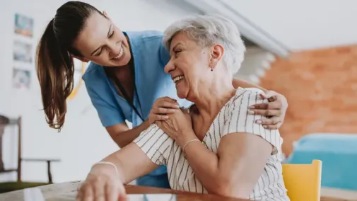 A woman and a carer sit at a table, laughing