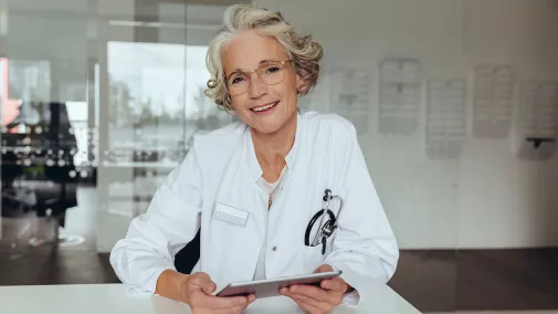 A doctor wearing a coat and glasses smiles.