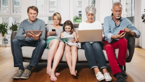 Familie mit Notebook und Smarthone sitzen auf Couch zu Hause
