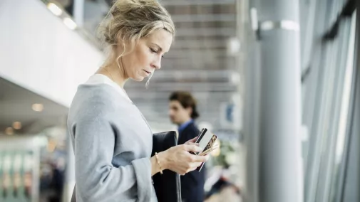 Frau mit Smartphone steht im Flughafengebäude