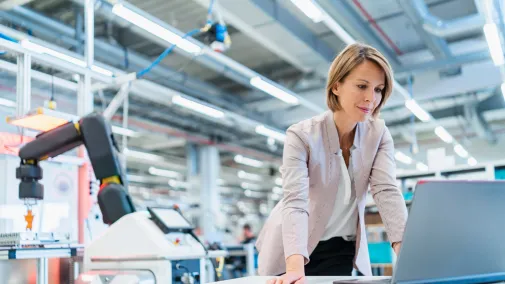 Frau steht am Notebook in Industriehalle