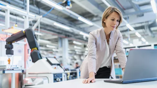 Frau steht am Notebook in Industriehalle