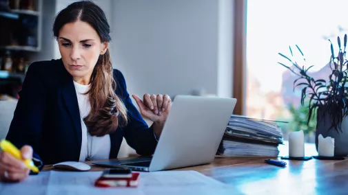 Frau mit Notebook am Tisch schreibt was auf und ist zu Hause