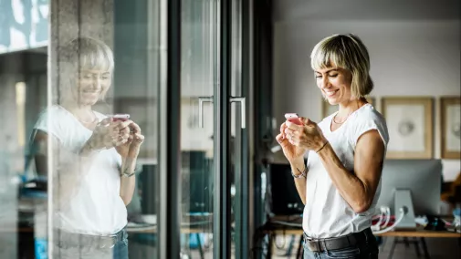 Frau schaut auf Smartphone und steht im Büro Frau schaut auf Smartphone und steht im Büro