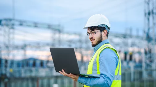 Mann mit Helm und Warnweste blickt in Computer