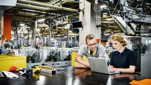 Frau und Mann vor einem Laptop in einer Industriehalle 