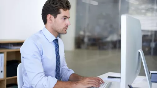 Mann sitzt am Computer am Tisch im Büro