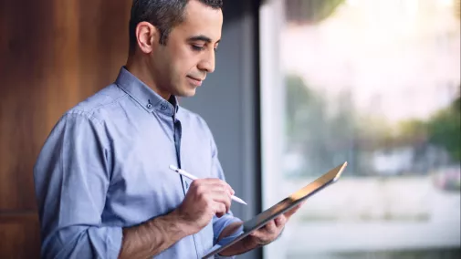 Mann steht mit Tablet und Stift im Büro am Fenster Mann steht mit Tablet und Stift im Büro am Fenster