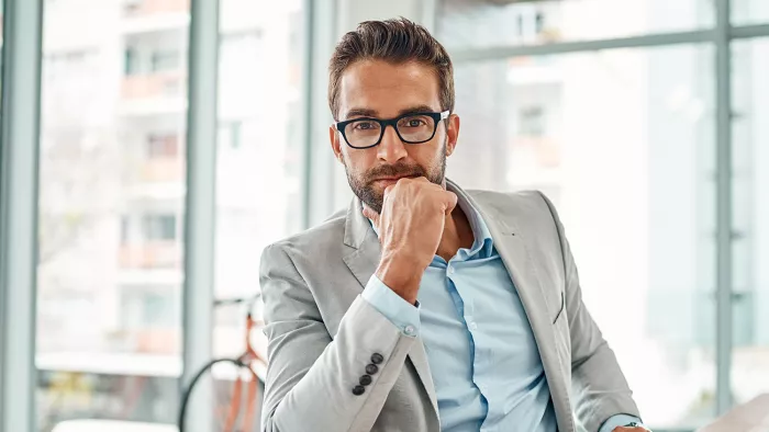 Mann mit Brille in Anzug sitzt nachdenklich im Büro