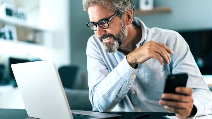 Mann mit Smartphone vor einem Laptop